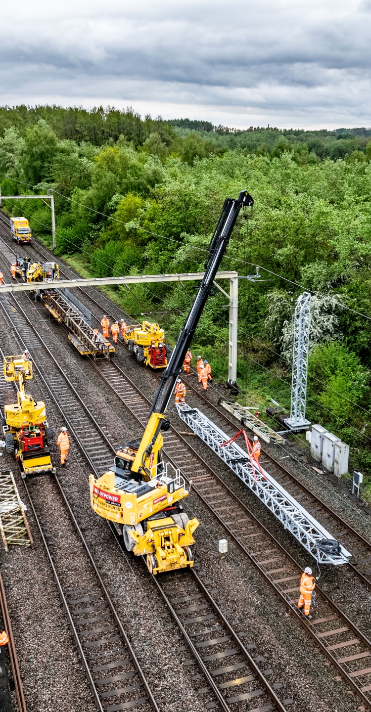 VolkerRail installing a gantry over track on a sunny day surrounded by trees