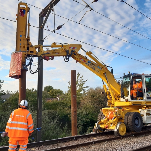 road rail vehicle with a piling hammer and a man in PPE watching
