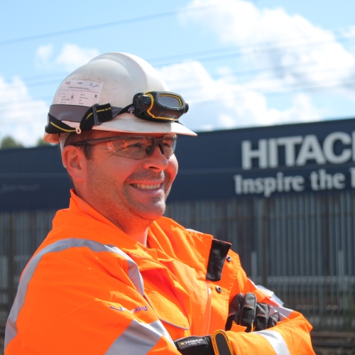 Man smiling with a Hitachi sign behind him