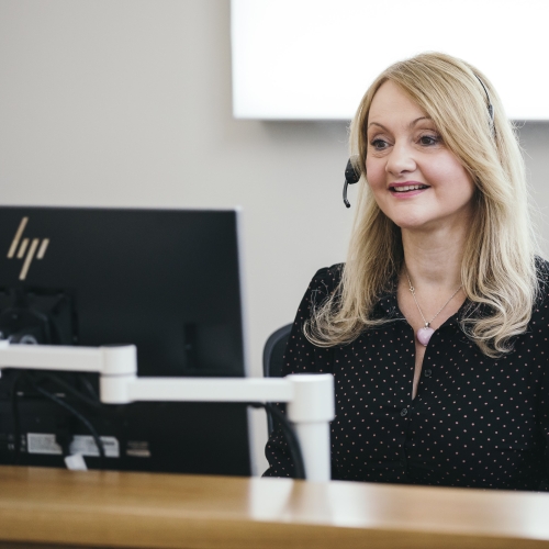 A women sat at her desk, wearing a headset 