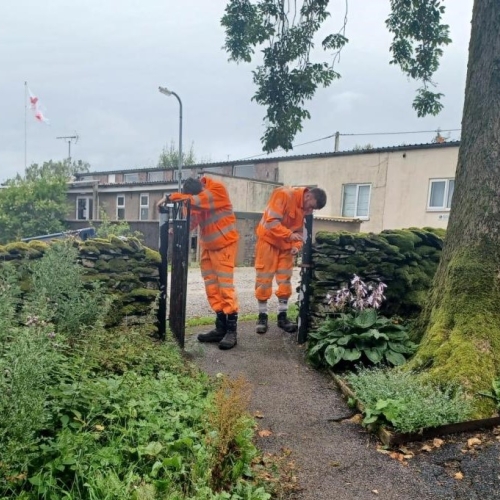 Two men in orange PPE paining an iron fence in a church yard