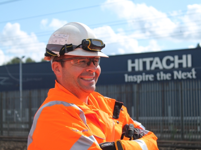 Man smiling with a Hitachi sign behind him