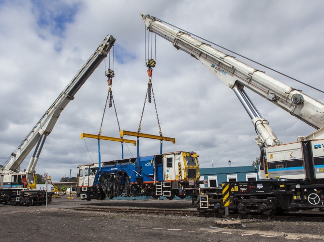 A beaver tamper being lifted onto track by two Kirow cranes working in tandem