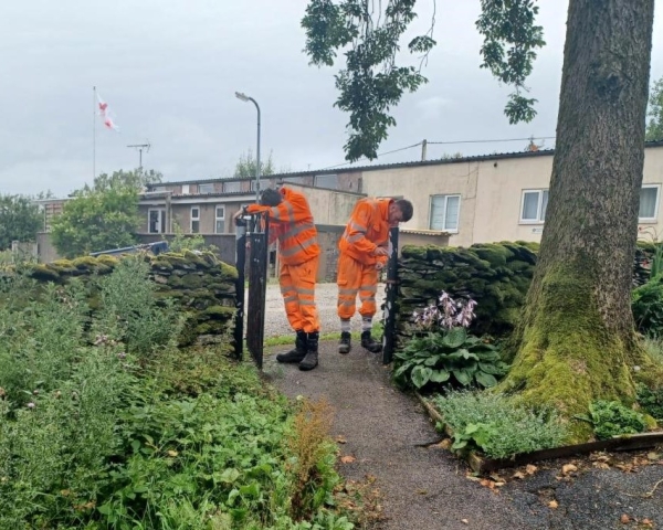 Two men in orange PPE paining an iron fence in a church yard