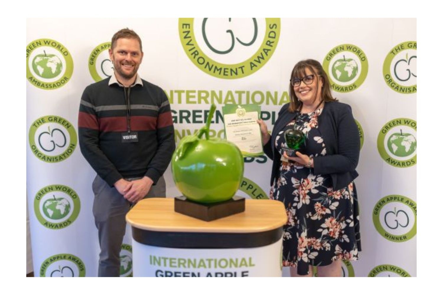two people collecting a green apple award, one man one women, both smiling