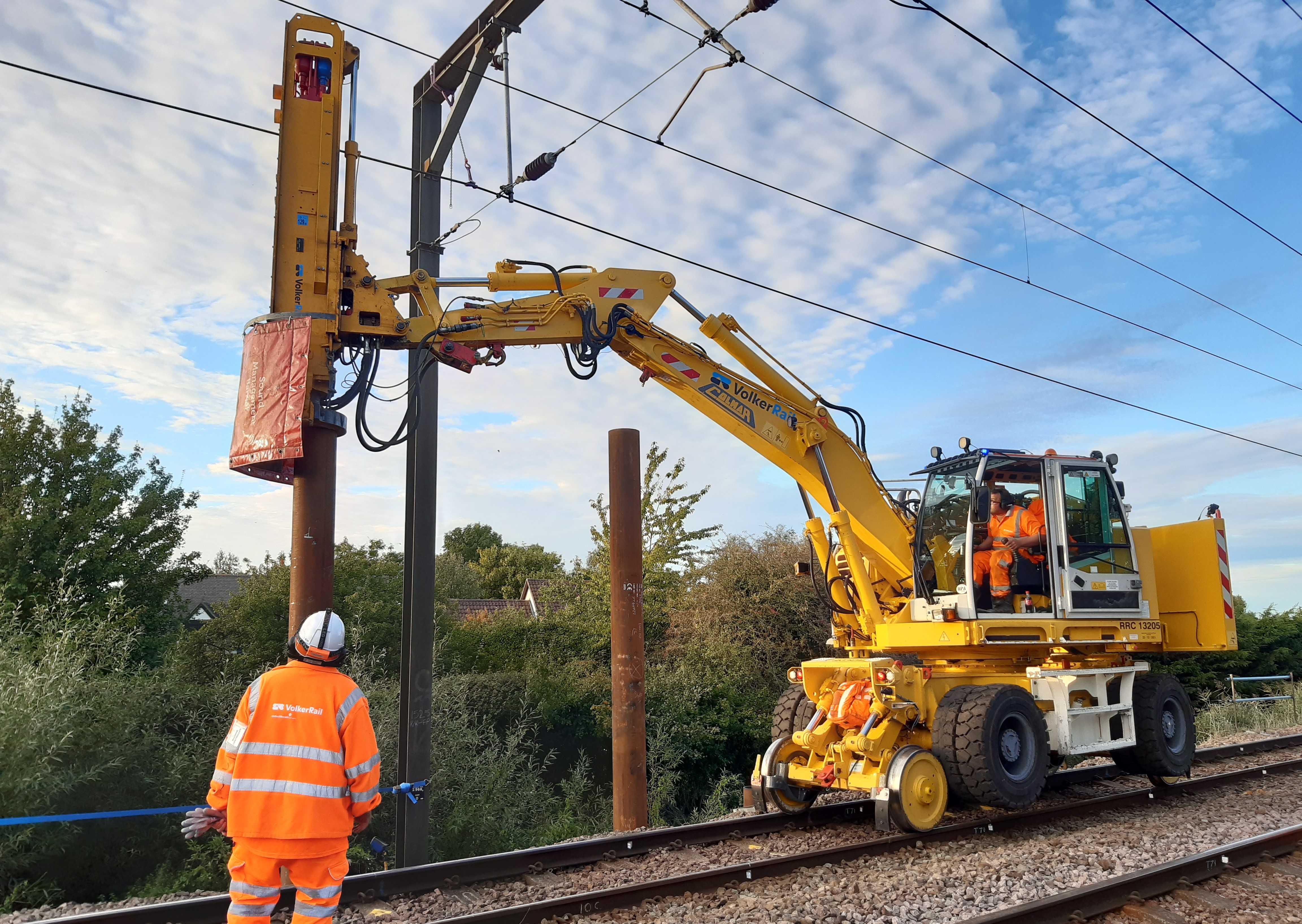 road rail vehicle with a piling hammer and a man in PPE watching