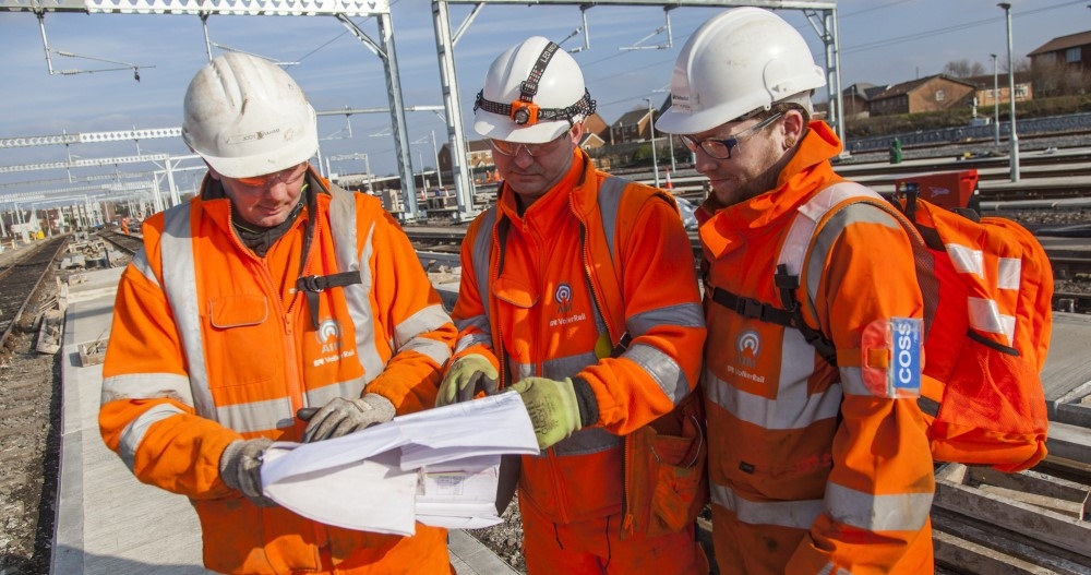 three men in orange PPE looking at paperwork on site