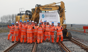 group of people in orange PPE with their thumbs up in front of a Komatsu crane and EWR sign